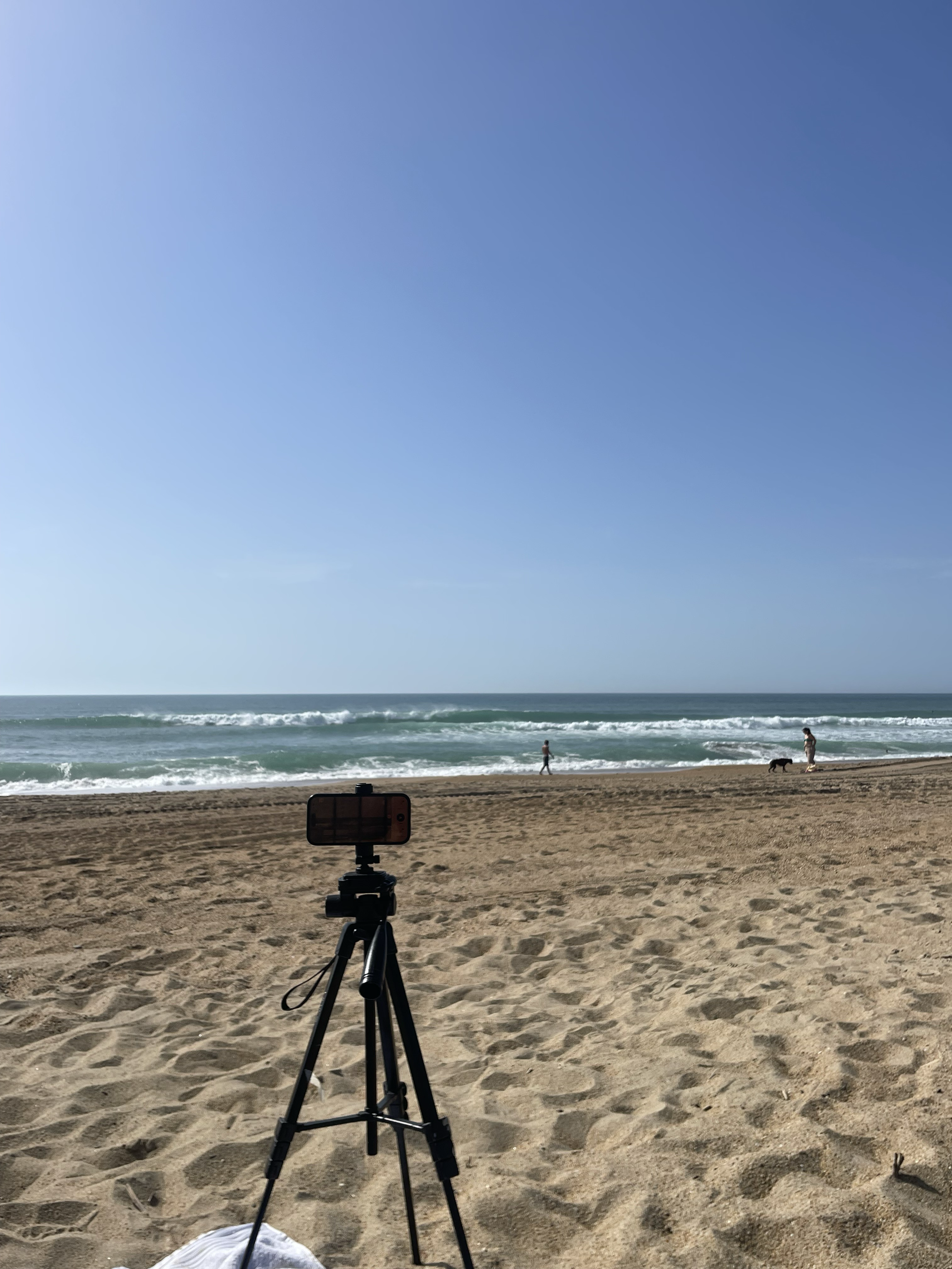 An iPhone mounted on a tripod on the beach, aimed at the surf